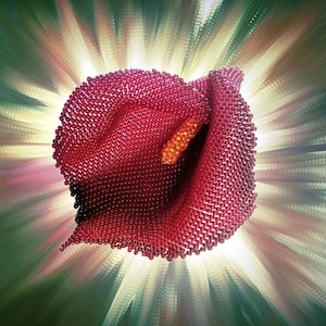 May include: A red, beaded calla lily sculpture with an orange stamen. The flower is set against a background of radiating light and metallic green and silver tones. The sculpture is a unique piece of art.