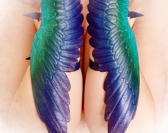 Par de brazaletes de cuero repujado con forma de alas de pavo real y brillo iridiscente arcoíris.