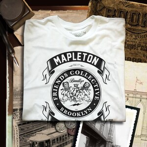 May include: A white t-shirt with a black and white graphic design featuring a crest with two lions, the text "Friends Collective", and the words "Mapleton Brooklyn".