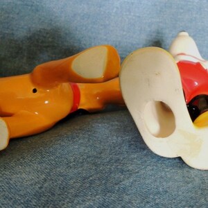 May include: Bottom view of two ceramic figurines, one of Mickey Mouse and one of Pluto. Mickey Mouse is wearing red shorts and yellow shoes. Pluto is orange and has the text "&copy;DISNEY CHINA" on the bottom.