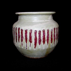 May include: A ceramic vase with a light green glaze and vertical red stripes. The vase has a rounded body and a slightly flared rim. The design is simple and elegant.