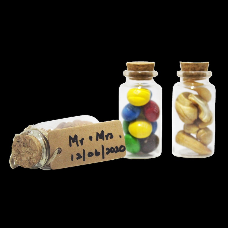 May include: Three small glass jars with cork lids, filled with colorful candies, nuts, and a tag that reads "Mr. & Mrs. 12/06/2020".
