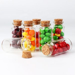 May include: A set of eight small glass bottles with cork stoppers filled with colorful candy. The bottles are clear glass and the candy is red, green, yellow, and orange.