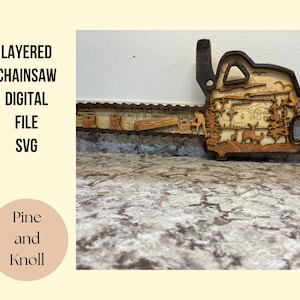 Puede incluir: Diseño de sierra de cadena de madera en capas con una escena detallada de un bosque, que incluye árboles, una cabaña y animales. El diseño está hecho para corte por láser y está disponible como un archivo SVG digital.