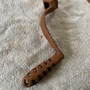 May include: A rusty cast iron hand crank with a square head and a handle with a perforated grip.