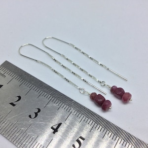 May include: A pair of silver dangle earrings with a chain and three pink gemstone beads. The earrings are measured against a ruler, showing they are approximately 3 inches long.