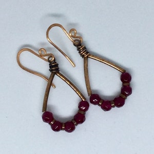 May include: A pair of teardrop-shaped earrings with a brass wire frame and burgundy beads.