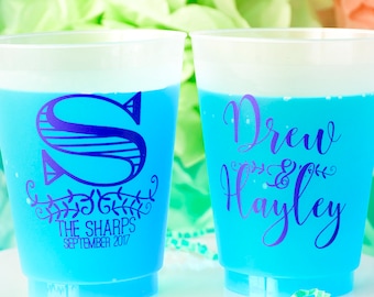 May include: Two blue plastic cups with white rims. The cup on the left has a purple "S" with a floral design and the text "The Sharps September 2017". The cup on the right has the text "Drew & Hayley" in purple.