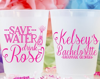May include: Two clear plastic cups with pink text. One cup says "...Save...Water drink Rosé" with a pink champagne bottle graphic. The other cup says "Kelsey's Bachelorette -Savannah, Georgia- ".