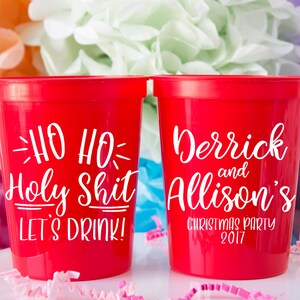 May include: Two red plastic cups with white text. One cup says "Ho Ho Holy Shit Let's Drink!" and the other cup says "Derrick and Allison's Christmas Party 2017".
