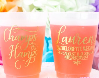 May include: Two clear plastic cups with pink liquid. One cup has gold lettering that says "Champs in the Hamps". The other cup has gold lettering that says "Lauren's Bachelorette Weekend August 11-13 2017 #hitchedtoapoast"