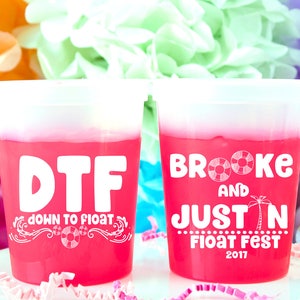May include: Two pink plastic cups with white text. The left cup says "DTF down to float" with a life preserver graphic. The right cup says "Brooke and Justin Float Fest 2017".