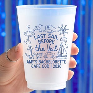 May include: A frosted plastic cup with a blue nautical design and the text "LAST SAIL BEFORE the VEIL". The cup also includes the text "AMY'S BACHELORETTE CAPE COD | 2026". The design features a sailboat, anchor, and other nautical elements.
