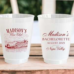 May include: Two white plastic cups with red text. The left cup says "Madison's Wine Club" with a drawing of a vineyard. The right cup says "Madison's Bachelorette August 2025 Napa Valley".