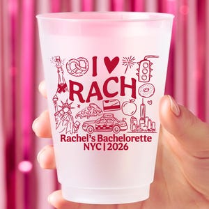 May include: A frosted plastic cup featuring red printed graphics including a pretzel, a heart, a traffic light, the Statue of Liberty, a pizza slice, a taxi, an apple, and the text I LOVE RACH, Rachel's Bachelorette, and NYC 2026.