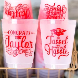 May include: Four red and white graduation party cups with the text "Congrats... Taylor Class of 2019", "2019 The Tassel Was Worth The Hassle", and "Class of 2019" on them. The cups are sitting on a gold wire rack.