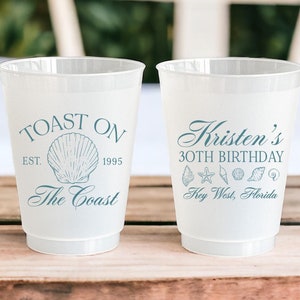 K&ouml;nnte beinhalten: Zwei wei&szlig;e Plastikbecher mit blauem Text und Illustrationen. Der linke Becher sagt "Toast On Est. 1995 The Coast" mit einer Muschel-Illustration. Der rechte Becher sagt "Kristen's 30th Birthday Key West, Florida" mit einem Seestern und Muscheln.