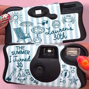 May include: Two disposable cameras with light blue and white vertical stripes. The top camera features a sun, umbrella, chair, shell, crab, and text reading Lauren's 30th. The bottom camera features text reading The Summer I Turned 30 Est. 1996, a bikini, champagne, and a starfish.