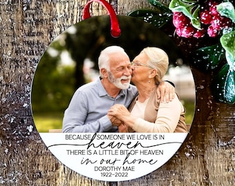 May include: A round white ornament with a photo of an older couple. The ornament has the text "Because someone we love is in heaven there is a little bit of heaven in our home Dorothy Mae 1922-2022".
