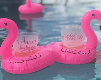 May include: Two pink inflatable flamingo pool floats with clear plastic cups in the center. The cups have text that reads "Anne's Bachelorette" and "Naples, FL 9/21/18".