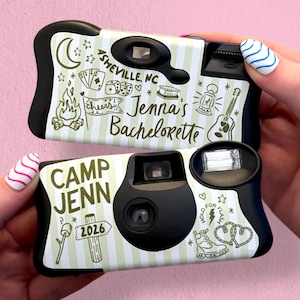 May include: Two black and white disposable cameras with green and white striped designs. One camera says "Jenna's Bachelorette" and the other says "Camp Jenn 2026". The cameras have camping-themed illustrations.