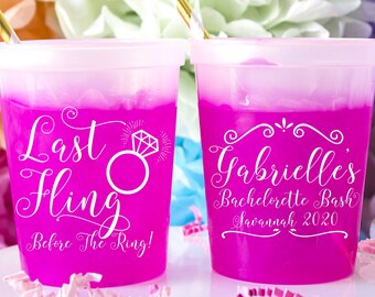 May include: Two pink plastic cups with white text. The cup on the left says "Last Fling Before The Ring!" with a diamond ring graphic. The cup on the right says "Gabrielles Bachelorette Bash Savannah 2020".