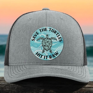 May include: A gray and black trucker hat with a circular patch featuring a black sea turtle with blue waves and the text "Save the Turtles Hit it Raw".