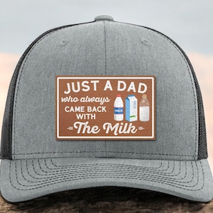 May include: Gray trucker hat with a black mesh back. The front features a brown patch with the text "JUST A DAD who always CAME BACK WITH The Milk" and illustrations of milk containers. A stylish accessory for any dad.