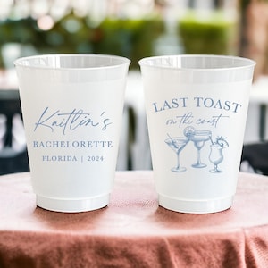 May include: Two white plastic cups with blue text and designs. One cup says "Kaitlin's Bachelorette Florida | 2024". The other cup says "Last Toast on the Coast" with a drawing of three cocktails.