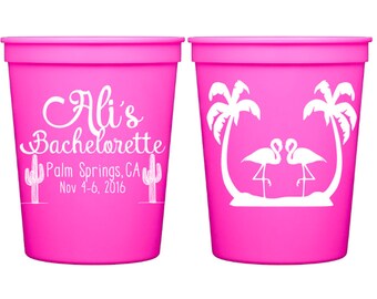 May include: Two pink plastic cups with white designs. One cup has the text "Ali's Bachelorette Palm Springs, CA Nov 4-6, 2016". The other cup has two flamingos and palm trees.