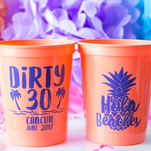 Może przedstawiać: Dwa pomarańczowe plastikowe kubki z niebieskim tekstem i wzorami. Jeden kubek ma napis "Dirty 30" z palmami i "Cancun Czerwiec 2017". Drugi kubek ma napis "Hola Beaches" z ananasem.