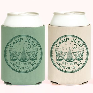 May include: Three cylindrical foam can coolers in sage green, beige, and dark forest green. Each features a circular graphic with the text CAMP JESS, ASHEVILLE, NC, EST. 2025, surrounding an illustration of two folding chairs and a campfire.