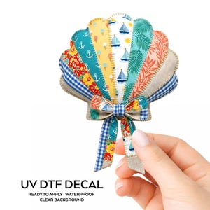 May include: A colorful seashell-shaped UV DTF decal with various patterned sections, including anchors, sailboats, and floral designs. The decal has a blue and white gingham bow and the text "UV DTF DECAL READY TO APPLY - WATERPROOF CLEAR BACKGROUND".