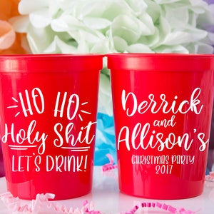 May include: Two red plastic cups with white text. One cup says "Ho Ho Holy Shit Let's Drink!" and the other cup says "Derrick and Allison's Christmas Party 2017".