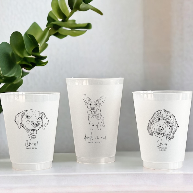May include: Three white plastic cups with black line drawings of dogs. One cup has a Labrador, another a Corgi, and the third a Goldendoodle. Text includes "Cheers!" and "Drinks on me!" with names below.