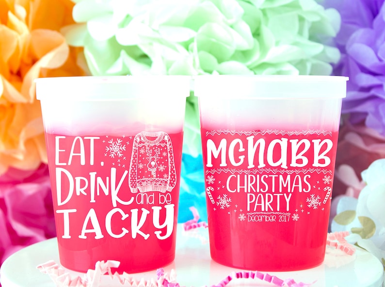 May include: Two pink plastic cups with white text. The first cup says "Eat, Drink and be Tacky" with a drawing of a Christmas sweater. The second cup says "McNabb Christmas Party December 2017".