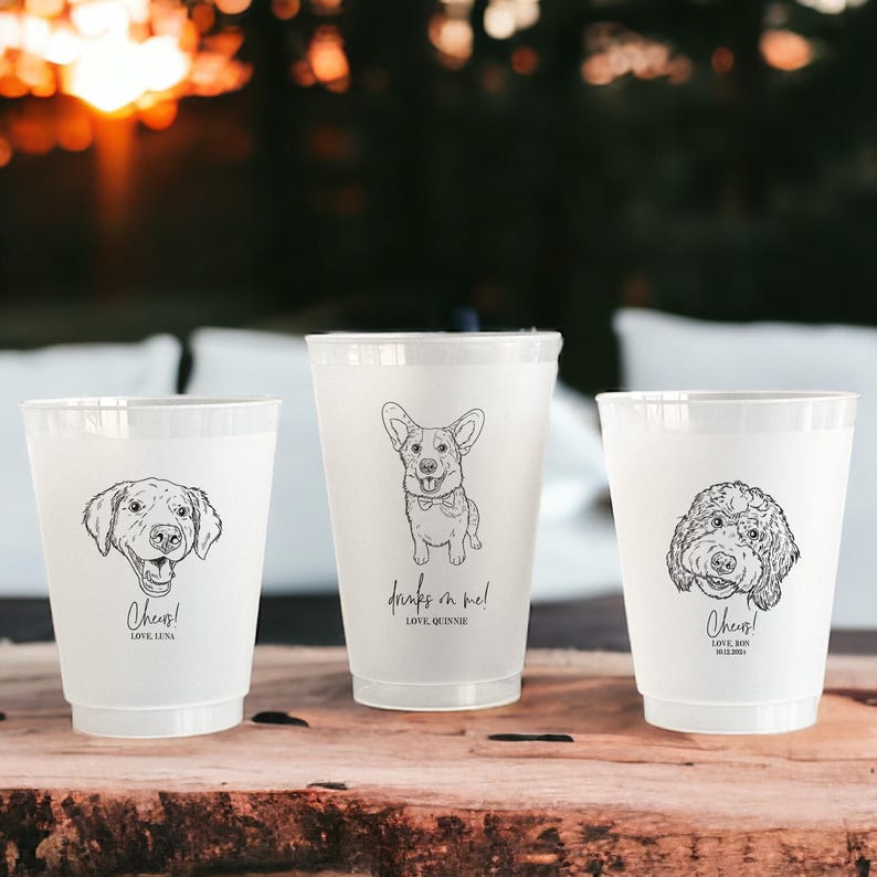 May include: Three white plastic cups with black line drawings of dogs. Each cup has a different dog breed illustration and text. The text on the cups reads "Cheers! Love Luna", "Drinks on me! Love Quinnie", and "Cheers! Love Rex".