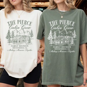 Pu&ograve; includere: Due magliette oversize, una color crema e una verde oliva, con una grafica di un rifugio di montagna e il testo "THE PIERCE Cabin Crew FAMILY REUNION BRECKENRIDGE, CO Making Memories Together". Le magliette sono indossate da una persona.