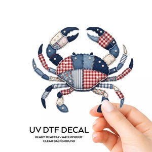 May include: A crab-shaped UV DTF decal with a patchwork design. The crab features a mix of denim, red gingham, and floral patterns, accented with small pearl-like embellishments. The text "UV DTF DECAL" is visible at the bottom.