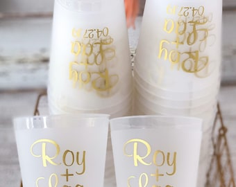 May include: White plastic cups with gold lettering. The cups are stacked and feature the names "Roy + Laa" and the date "04.27.19".
