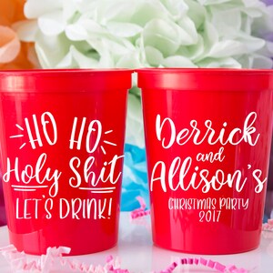 May include: Two red plastic cups with white text. One cup says "HO HO Holy Shit Let's Drink!" and the other cup says "Derrick and Allison's Christmas Party 2017".