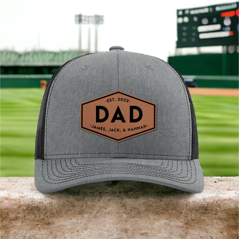 May include: Gray and black trucker hat with a brown leather patch that says "DAD -EST. 2022- JAMES, JACK, & HANNAH"