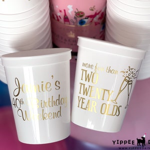 May include: Two white plastic cups with gold lettering. One cup says "Jamie's 40th Birthday Weekend" and the other says "More fun than two twenty year olds".