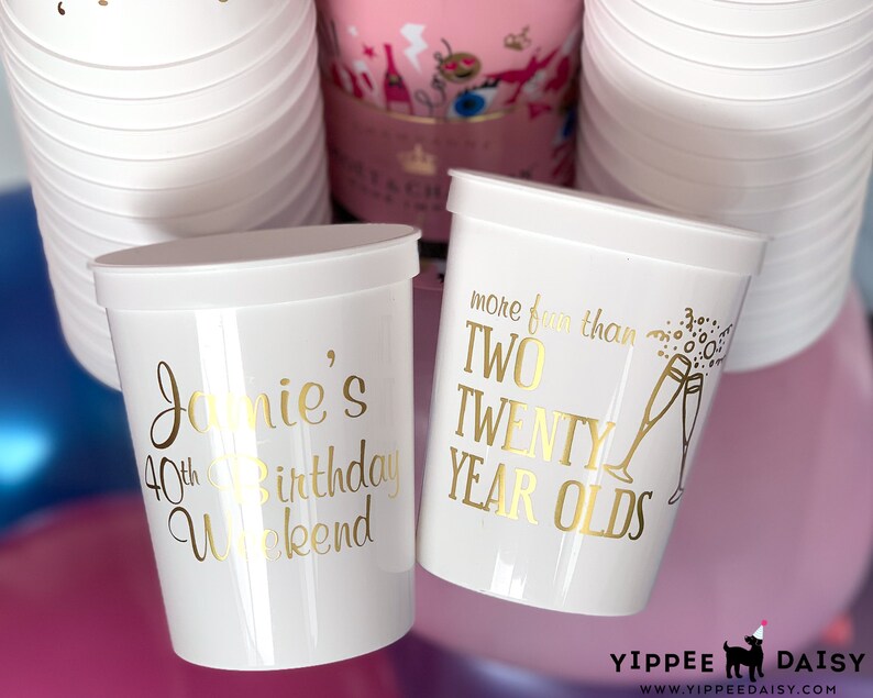 May include: Two white plastic cups with gold lettering. One cup says "Jamie's 40th Birthday Weekend" and the other says "More fun than two twenty year olds".