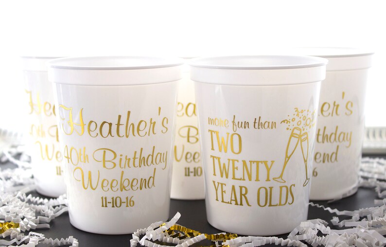 May include: Four white plastic cups with gold lettering. The cups are decorated with the text "Heather's 40th Birthday Weekend 11-10-16", "more fun than two twenty year olds", and "Heather's birthday weekend".
