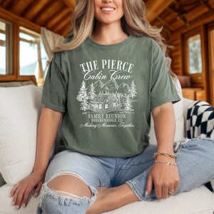 Pu&ograve; includere: T-shirt verde oliva con testo e illustrazione bianchi. Il testo recita "THE PIERCE CABIN CREW FAMILY REUNION BRECKENRIDGE, CO Making Memories Together." L'illustrazione raffigura una baita, alberi e montagne. La maglietta &egrave; indossata.