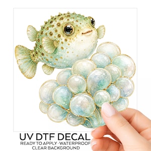 May include: A UV DTF decal featuring a light green pufferfish with gold accents and large dark eyes, positioned above a cluster of translucent, pale blue and green bubbles with gold outlines. The text reads UV DTF DECAL READY TO APPLY WATERPROOF CLEAR BACKGROUND.