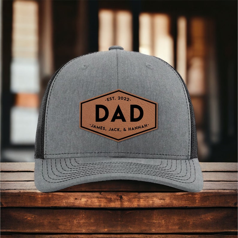 May include: Gray and black trucker hat with a brown leather patch that says "EST. 2022 - DAD - JAMES, JACK, & HANNAH"