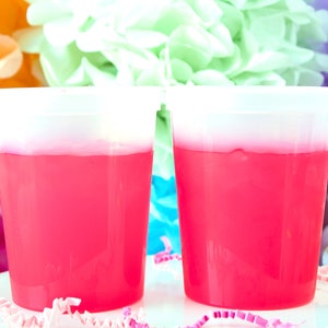 May include: Two clear plastic cups filled with bright pink slime, sitting on a white surface with colorful confetti.