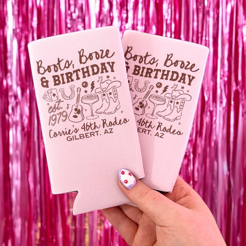 May include: Two pink can coolers with the text "Boots, Booze & Birthday" and a graphic of cowboy boots, a guitar, and a horseshoe. The text "Corrie's 46th Rodeo" and "Gilbert, AZ" are also printed on the coolers.